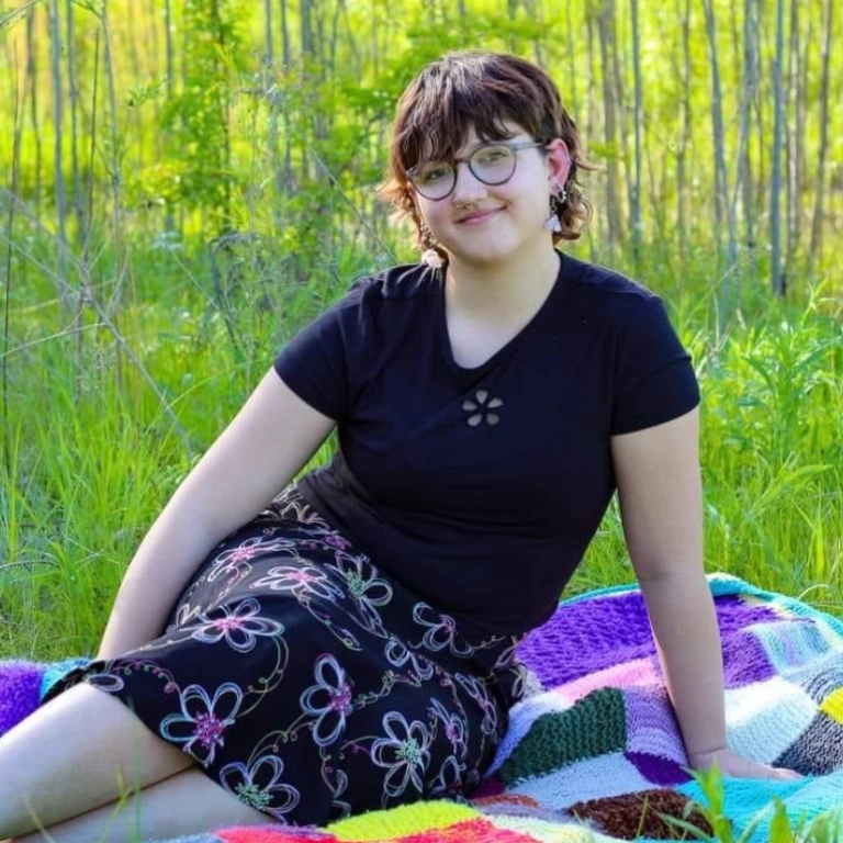 A student in a floral outfit sits in a meadow