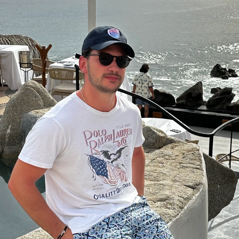 A student in a tshirt and sunglasses lounges at a rocky beachfront restaurant